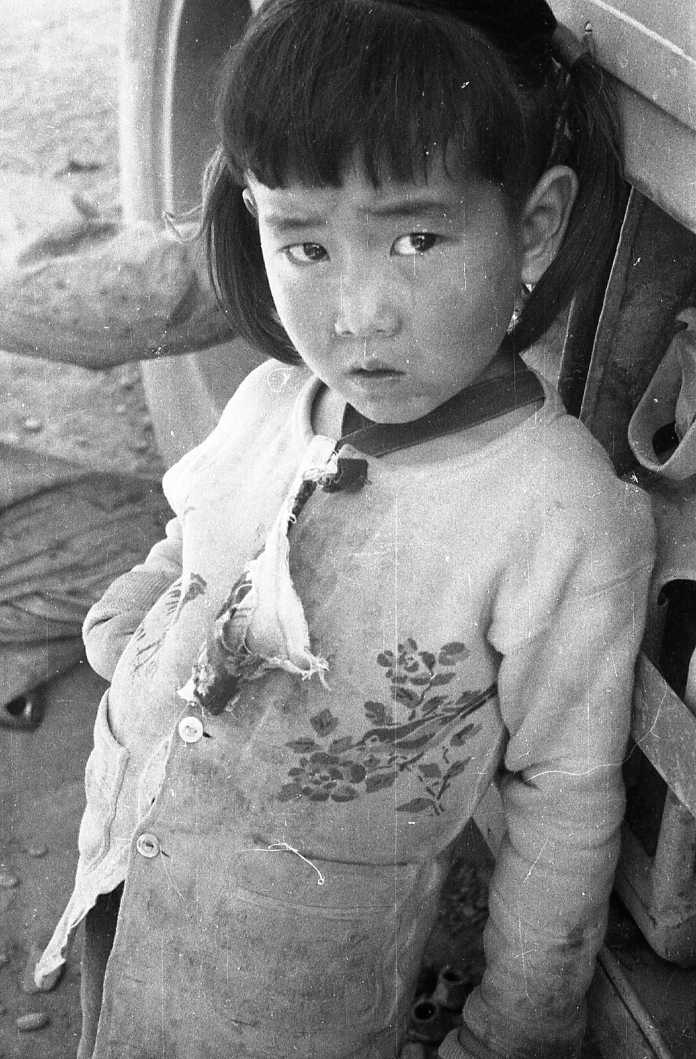 A young girl in a padded jacket looks at the camera, China, 1959.