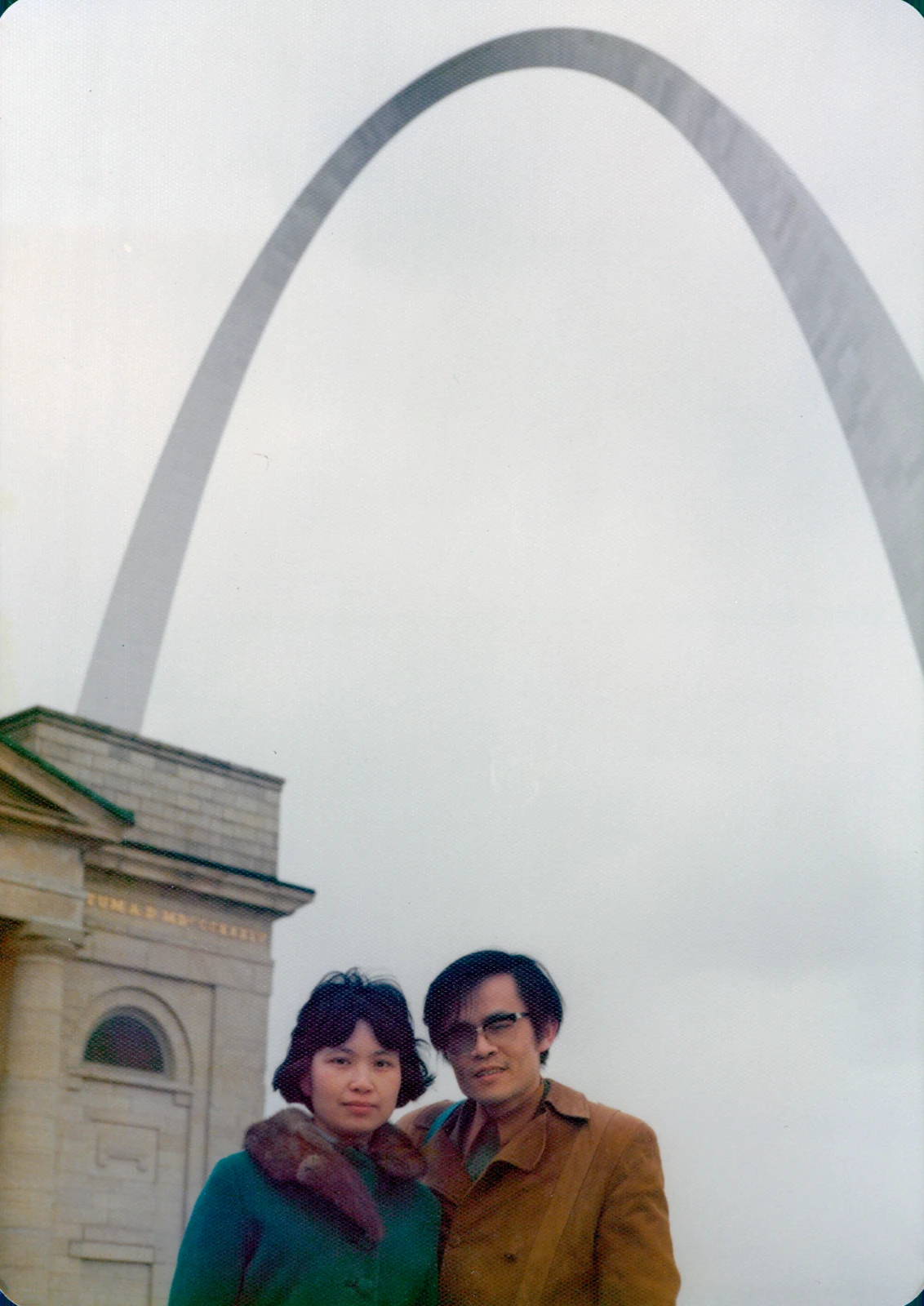 Esther and David stand close together beneath the Gateway Arch in St. Louis.